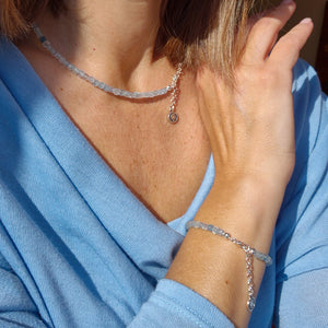 Person wearing a necklace and bracelet with a blue aquamarine