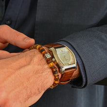 Load image into Gallery viewer, Close-up of a person wearing a gold watch and amberbracelet on a dark suit background