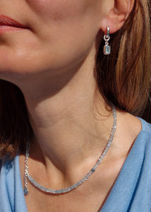 Close-up of a woman wearing a silver necklace and earrings with a blue top.